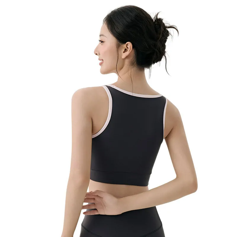 a sports bra. The model has dark, slightly tousled long hair falling over her shoulders. The bra is in a slate blue or dusty blue color with distinct off-white contrast piping that outlines the U-shaped neckline and straps.