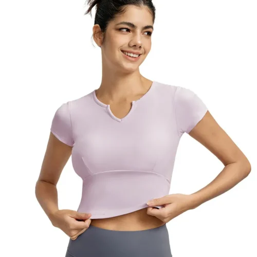 a light pink short-sleeve V-neck top. The fitted top features a subtle curved notch detail at the neckline, emphasizing the stretchy fabric.