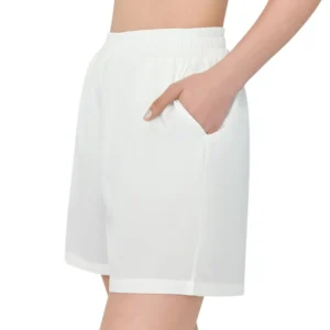 A woman's hand sliding into the pocket of a pair of white mid-thigh casual shorts, highlighting the pocket detail and soft drape of the fabric