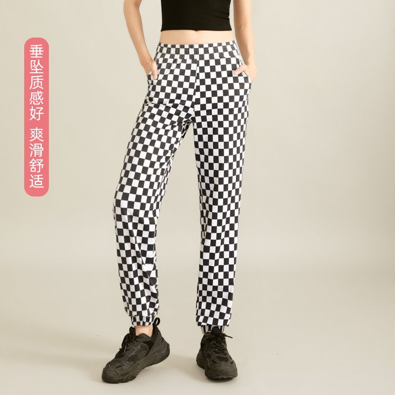 a black crop top and high-waisted black-and-white checkered flared pants, posing with hands in pockets.