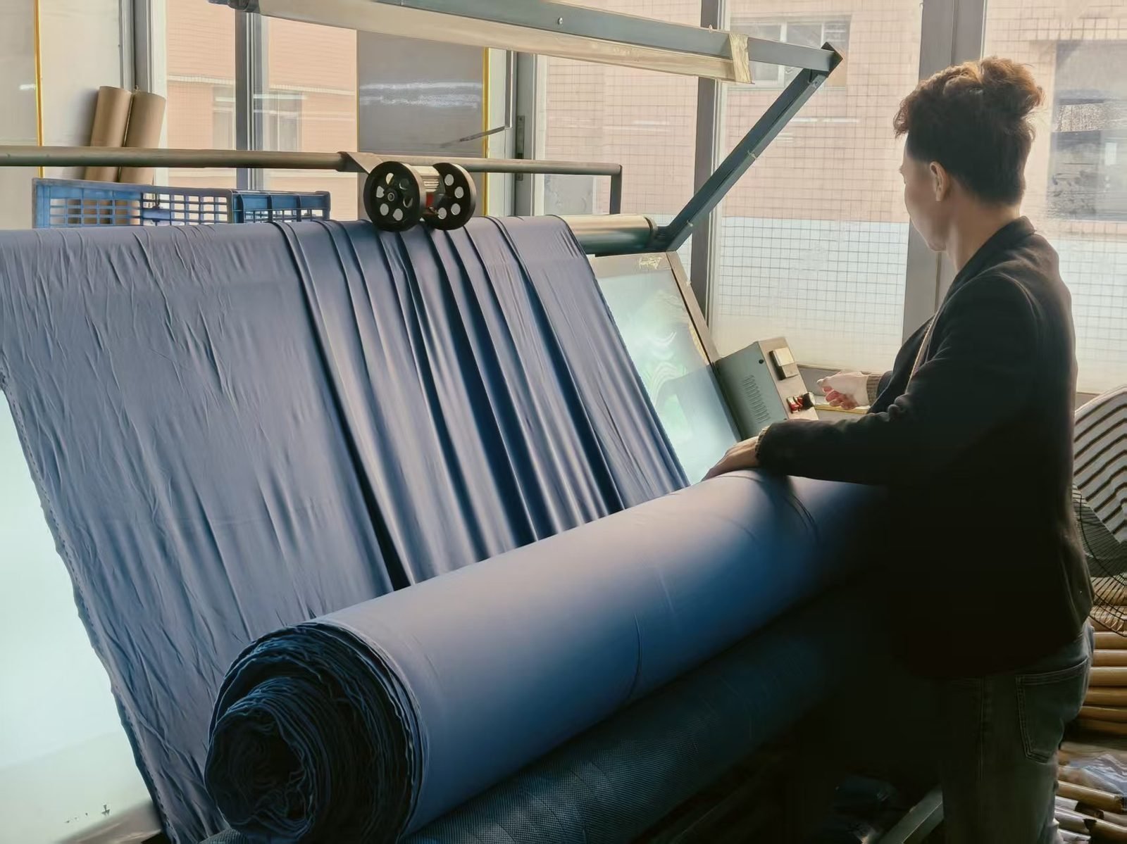 Worker inspecting a roll of blue swimwear fabric on a fabric inspection machine before cutting